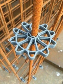 Grijze kunststof spacer gemonteerd op een roestvrijstalen staaf in een constructieomgeving met zichtbare steigers.