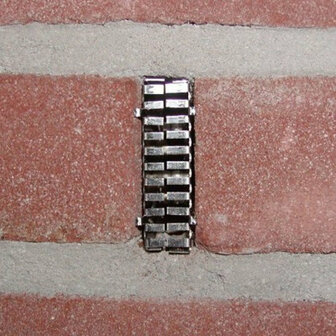 Glinsterend metalen clipje bevestigd aan een rode bakstenen muur, met een strakke, rechte structuur.