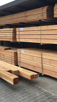 Houten planken in warme tinten, stapels op een metalen rek, met groene logo&#039;s en duidelijke labels aan de zijkanten.