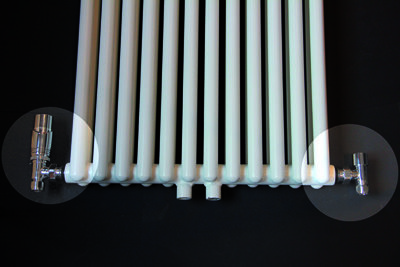 Witte verwarming met verticale buizen en metalen ventielen aan beide uiteinden op een zwarte achtergrond.
