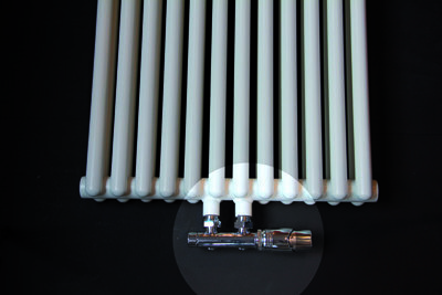 Witte radiator met verticale buizen en een chroomkleurige thermostaatkraan aan de onderzijde op een zwarte achtergrond.