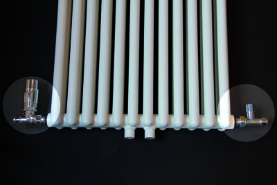 Witte rechte radiator met glanzende metalen ventielen aan beide uiteinden, geplaatst op een zwarte achtergrond.