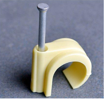 Geel plastic kabelclip met een metalen spijker in het midden, geplaatst op een grijze ondergrond.