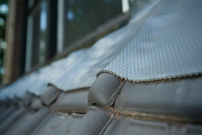 Een close-up van een grijze dakbedekking met een metalen rand en een zichtbare structuur, tegen een vervaagde achtergrond.