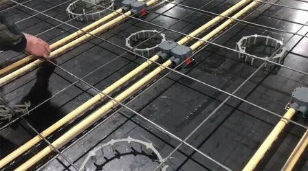 Een hand monteert plastic buizen en elektrische dozen op een zwarte, metalen ondergrond met stevige stalen staven.