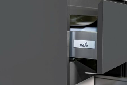 Grijze keukenlade met een Hettich logo op de voorkant, elegant en modern design met strakke lijnen.