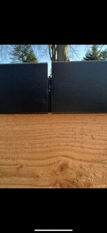 Zwarte metalen platen bovenop een houten ondergrond, met een naad in het midden en groene bomen op de achtergrond.