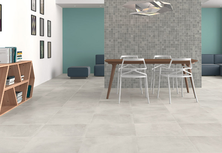 Lichte, grijze tegels op de vloer met een houten eetkamertafel en witte stoelen, tegen een groene muur met een tegelwand.