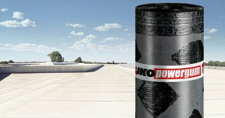 Een rol zwart dakbedekking met een patroon van ruiten staat op een vlakken dak onder een heldere blauwe lucht.