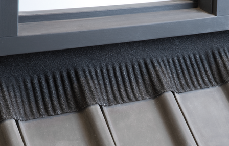 Zachte zwarte rand met verticale ribbels, geplaatst bovenop grijze tegel en naast een houten vensterkozijn.