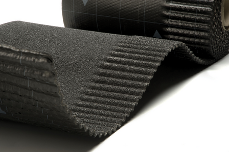 Zwarte rubberen mat met ribbelstructuur en een gladde achterkant, gedeeltelijk uitgerold op een witte ondergrond.
