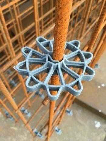 Grijze kunststof spacer gemonteerd op een roestvrijstalen staaf in een constructieomgeving met zichtbare steigers.