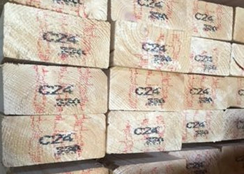 Stapels ongeverfd hout met zichtbaar merkteken 'C24' in zwart en rood, zorgvuldig gerangschikt op een lichte acht