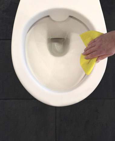 Witte toiletpot met een hand die een gele doek tegen de binnenrand aanhoudt, op een donkere tegelvloer.