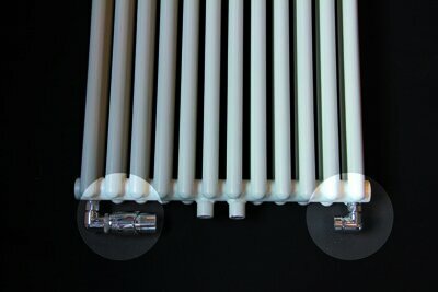 Langwerpige, witte radiator met metalen aansluitingen aan de onderkant, tegen een zwarte achtergrond.