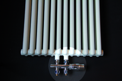 Rechthoekige, witte radiator met metalen aansluitingen, geplaatst op een zwarte ondergrond.