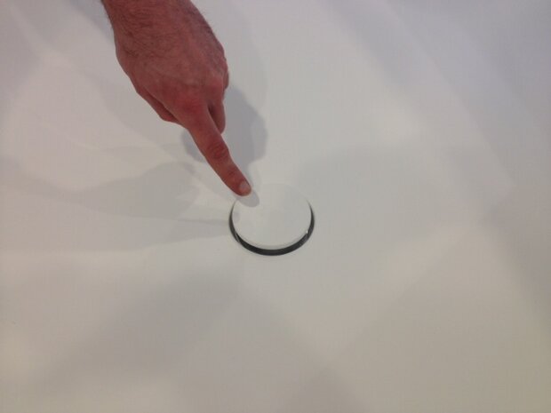 Een hand wijst op een witte, ronde knop met een zwarte rand op een witte ondergrond.