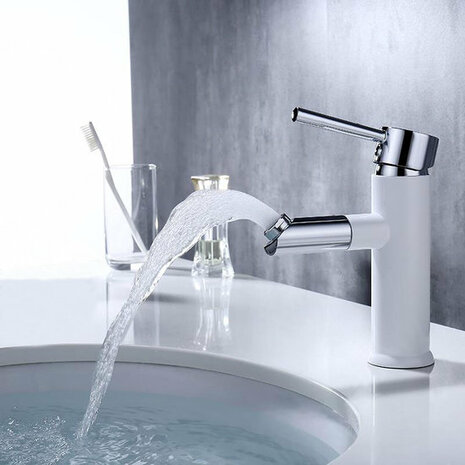 Glanzende chromen kraan met witte basis, die helder water in een ronde wasbak laat stromen, naast een glazen tandenborstelhouder.