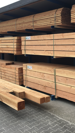 Rijen glad geschaafd houten planken in verschillende lengtes, gestapeld op metalen rekken op een betonnen vloer.