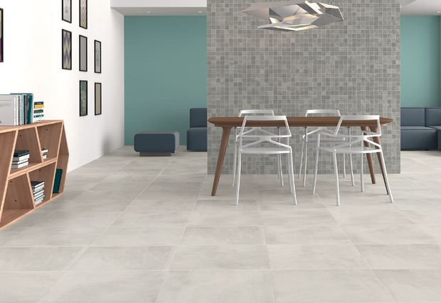 Lichte, grijze tegels op de vloer met een houten eetkamertafel en witte stoelen, tegen een groene muur met een tegelwand.