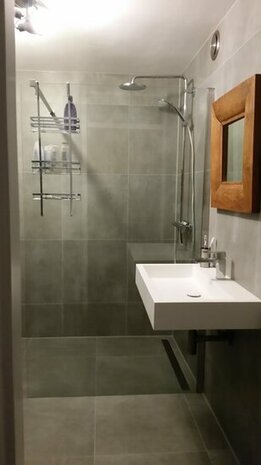 Moderne badkamer met grijze tegels, een zwevend wastafelmeubel en een houten spiegel in een strakke, minimalistische stijl.