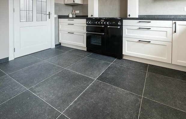 Moderne keuken met zwarte tegels, witte kasten en een klassieke zwarte oven in het midden. Lichtinval van de zijdeur.