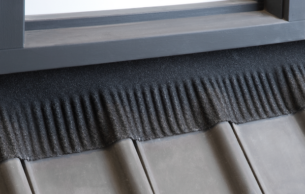 Zwarte dakpan met geribbelde bovenrand, in een moderne stijl, geplaatst tegen een grijze houten raamkozijn.